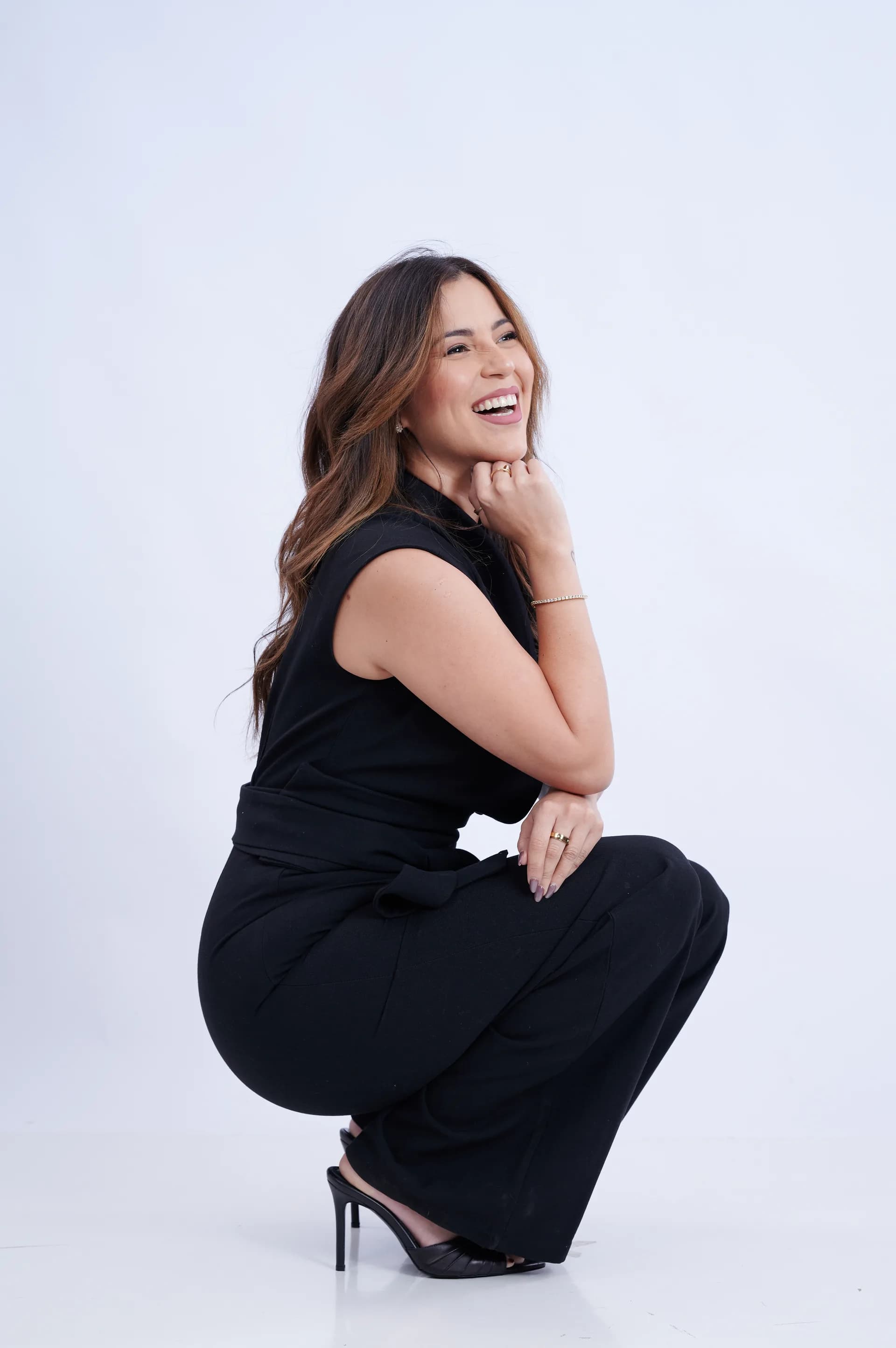 Stephanie Prentice en cuclillas, riendo, vestida de negro sobre fondo blanco